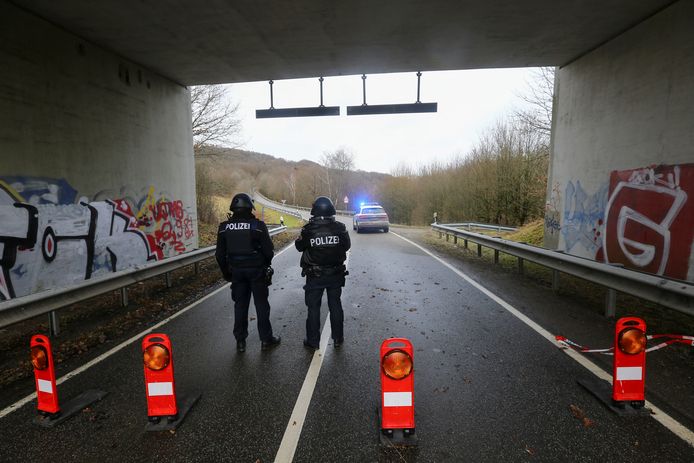 Zwaarbewapende politieagenten bewaken de weg naar de plaats delict.