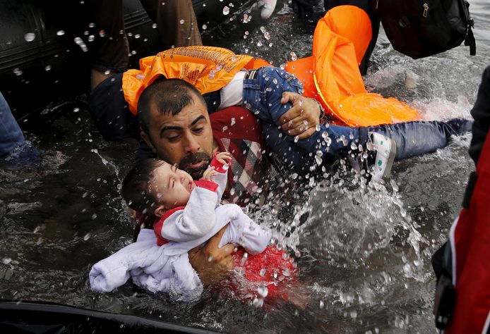 Een Syrische vluchteling houdt zijn kinderen vast om van een rubberboot op het Griekse eiland Lesbos te lopen.