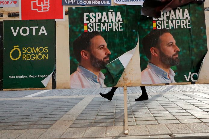 Een vrouw loopt achter posters van het extreemrechtse VOX, met een afbeelding van Santiago Abascal, langs.
