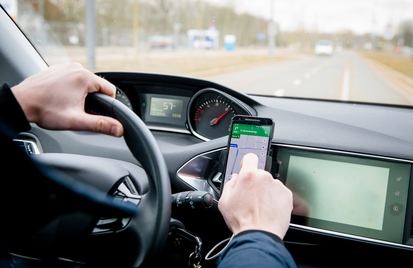 Een automobilist stelt de navigatie van zijn telefoon in tijdens het rijden.