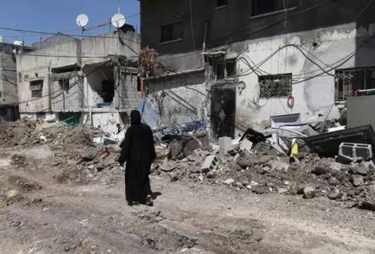 Een Palestijnse vrouw loopt langs een beschadigde weg na een aanval van het Israëlische leger in de Westelijke Jordaanoever-stad Tulkarem.