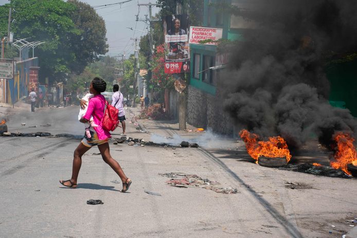 Een vrouw met een baby in haar armen zoekt een veilig heenkomen te midden van een schotenwisseling en brandende autobanden in de Haïtiaanse hoofdstad Port-au-Prince.