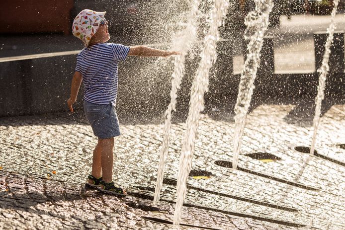 Een kind speelt in het water van de fontein op de Grote Markt van Ieper tijdens de warmste dag ooit.