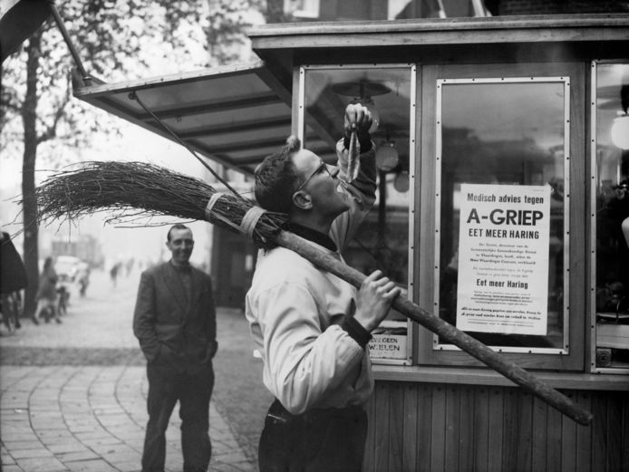 Een straatveger in Vlaardingen volgt het medisch advies tegen de A-griep op. Een rauwe haring zou wonderen doen. Menig AD-lezer weet zich de pandemie van 1957 nog goed te herinneren