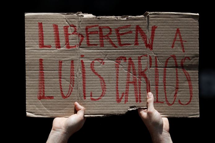 Een man houdt een stuk karton omhoog met daarop de tekst ‘laat Luis Carlos vrij’.
