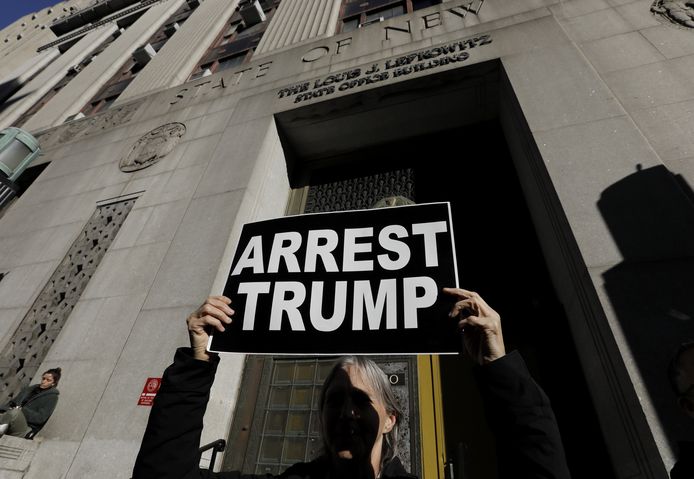 Een vrouw houdt in New York een bord omhoog met de tekst ‘arresteer Trump’.