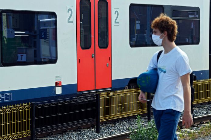 Een man met mondkapje op wacht op de trein.