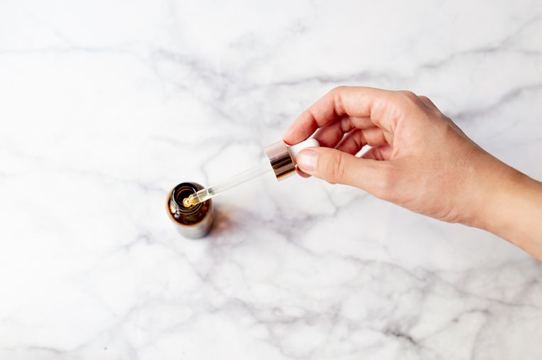 Top view of hand holding a retinol oil serum pipette and oil bottle on isolated marble background. Beauty care concept. Beeld Getty Images/500px Plus