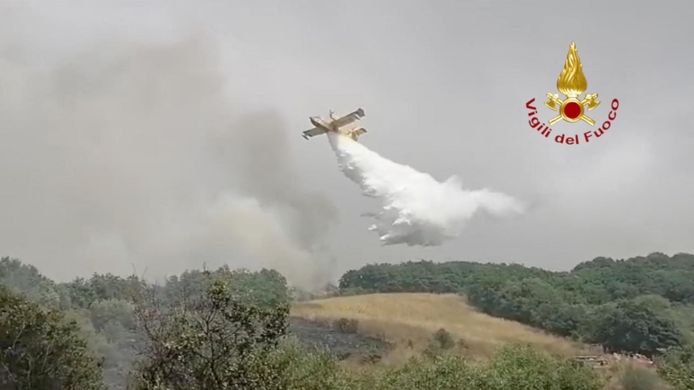 Een blusvliegtuig dumpt water op een bosbrand bij de stad Oristano.