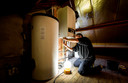 Een installateur is bezig met het installeren van een warmtepomp bij een verwarmingsketel, als onderdeel van een project om een jaren 60-woning energiezuinig te maken.