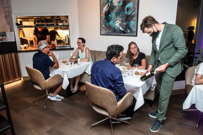 Gastheer Bono van Veelen geeft gasten uitleg over een wijn. Op de achtergrond chef-kok Niels van Kooten in de keuken.