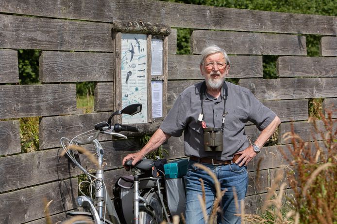 Op zijn tochten om vogels te kijken neemt Wim Smeets altijd de fiets mee. Hier staat hij achter de vogelkijkmuur naast de oeverzwaluwwand. De Gouden Lepelaar zit op zijn vestzakje, net naast het verrekijkerkoord.