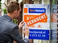 Een makelaar plakt een sticker 'verkocht' op een verkoopbord bij een woning in Delft.