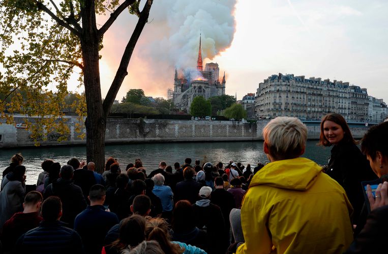 Mensen in Parijs hebben zich verzameld om te bidden en stil te staan bij de kerk die in brand staat. Beeld AFP