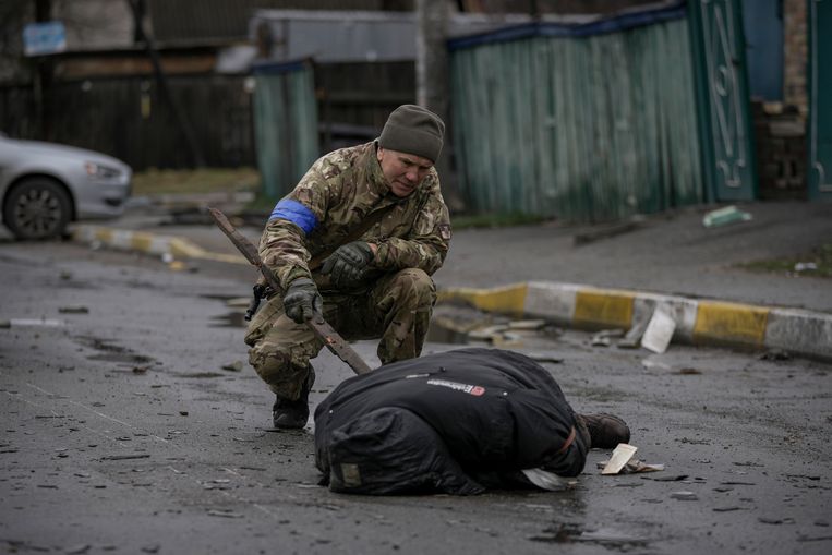 Een Oekraïense soldaat controleert of er geen explosieven aan een lichaam van een gedode burger bevestigd zijn. Beeld AP
