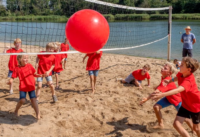Kinderen van de Kindervakantieweek spelen beachvolley aan de plas van het Wylerbergmeer. Het water zelf is, vanwege blauwalg, taboe voor de deelnemers.