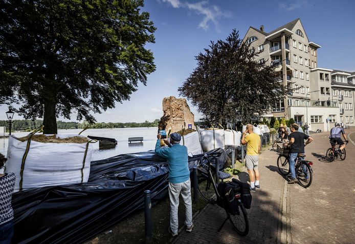Toeristen bekijken de opgestapelde zandzakken en het stijgende water van de Maas in het geëvacueerde Arcen vorige maand.