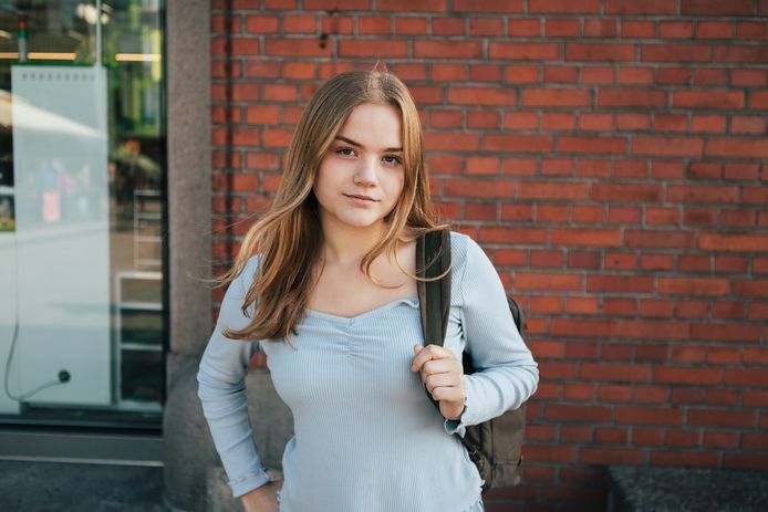 Portrait of a teenage girl standing in front of a brick wall.
