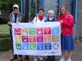Schepen Myriam Maes en enkele leden van het GROS houden trots de SDG-vlag vast.