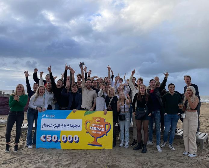 Het team van Grandcafé De Dominee op het strand in Scheveningen, waar de cheque ter waarde van 50.000 euro in ontvangst werd genomen.