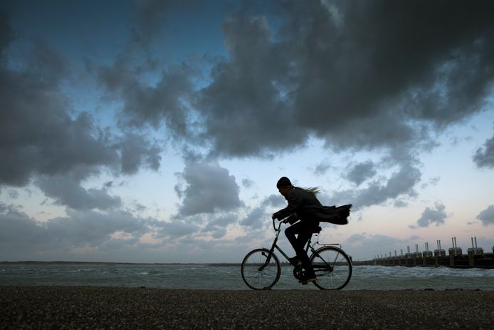 Een vrouw in Zeeland trotseert op de fiets de storm. Op de achtergrond de Oosterscheldekering.