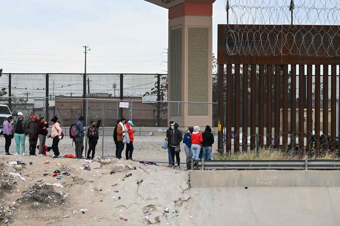 Een stuk grensmuur met ernaast migranten die zich overgeven aan Amerikaanse grensagenten in El Paso, Texas.
