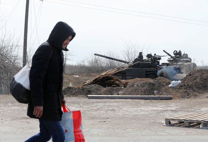 Een man loopt voor Russische tanks langs aan de stadsrand van Marioepol.
