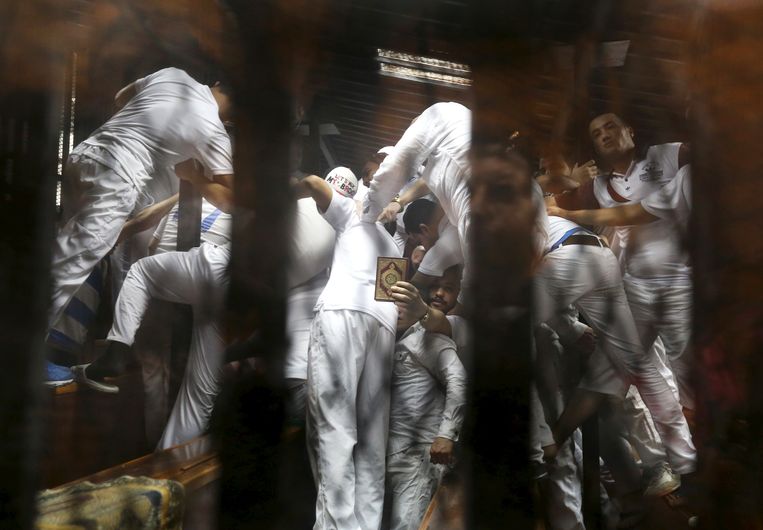 Een wirwar van gedaagden bidt met de Koran in de hand in de rechtbank in Cairo.  Beeld REUTERS