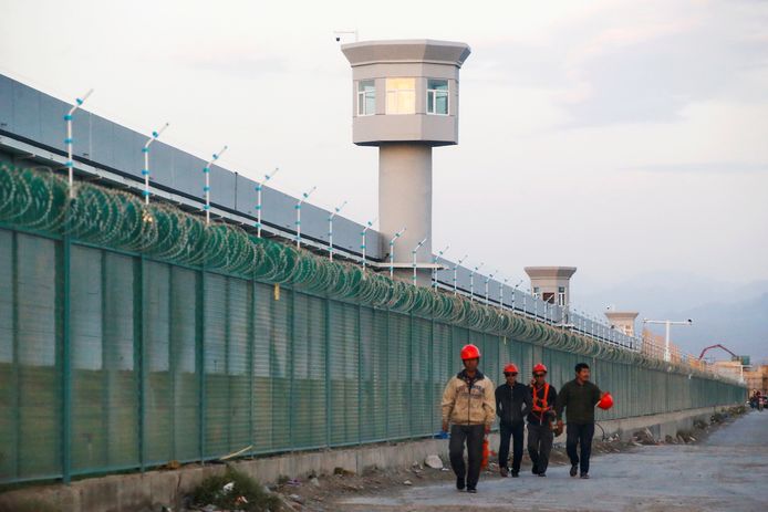 Arbeiders wandelen voorbij de omheining van een Oeigoerenkamp in China.