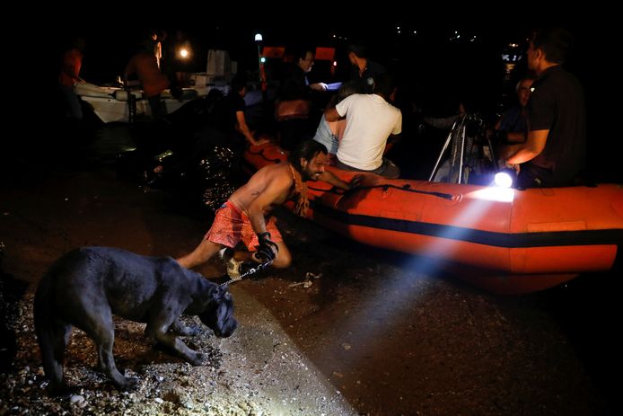 Een man met een hond duwt een opblaasboot waar dorpelingen uit Mati mee geëvacueerd worden weg van de waterkant.