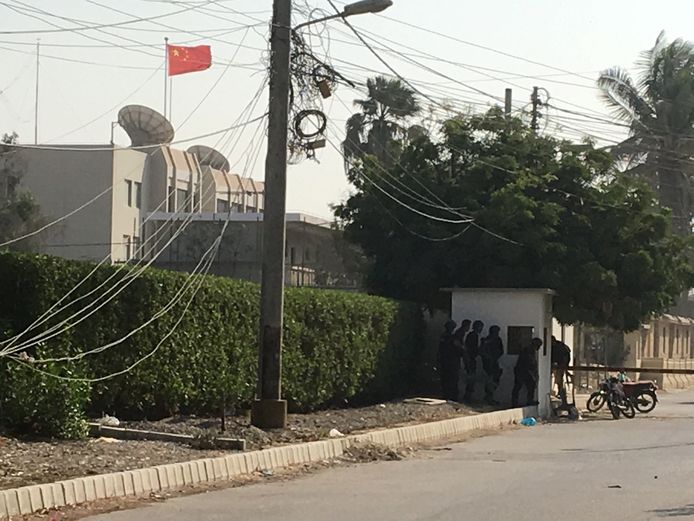 Paramilitairen en politieagenten zoeken beschutting achter een muurtje tijdens de aanval op de Chinese ambassade in Karachi in Pakistan.