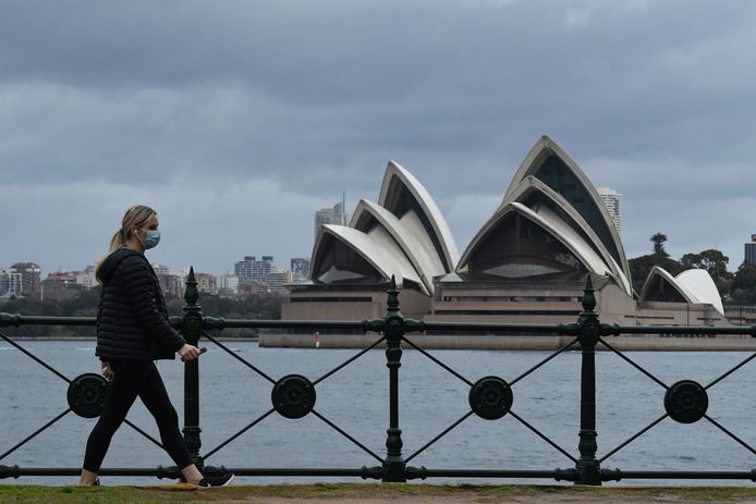 Een vrouw loopt voor het Sydney Opera House langs in Sydney, Australië.