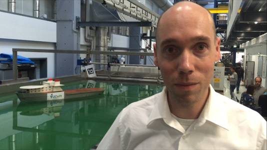 Onderzoeker Rudy Negenborn van de TU Delft. Op de achtergrond het modelrobotschip waar hij en zijn collegas onderzoek mee doen.