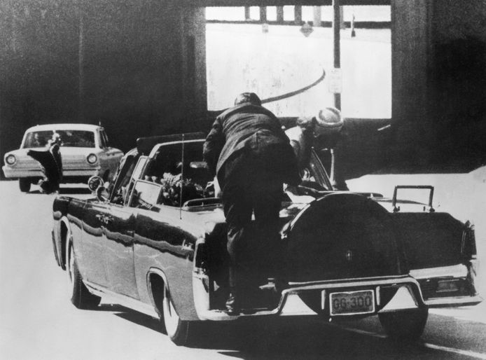 First Lady Jacqueline Kennedy bends over her distressed husband as a security person enters the car.