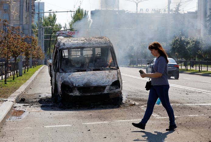 Een vrouw wandelt voorbij een voertuig dat vuur vatte in Donetsk.