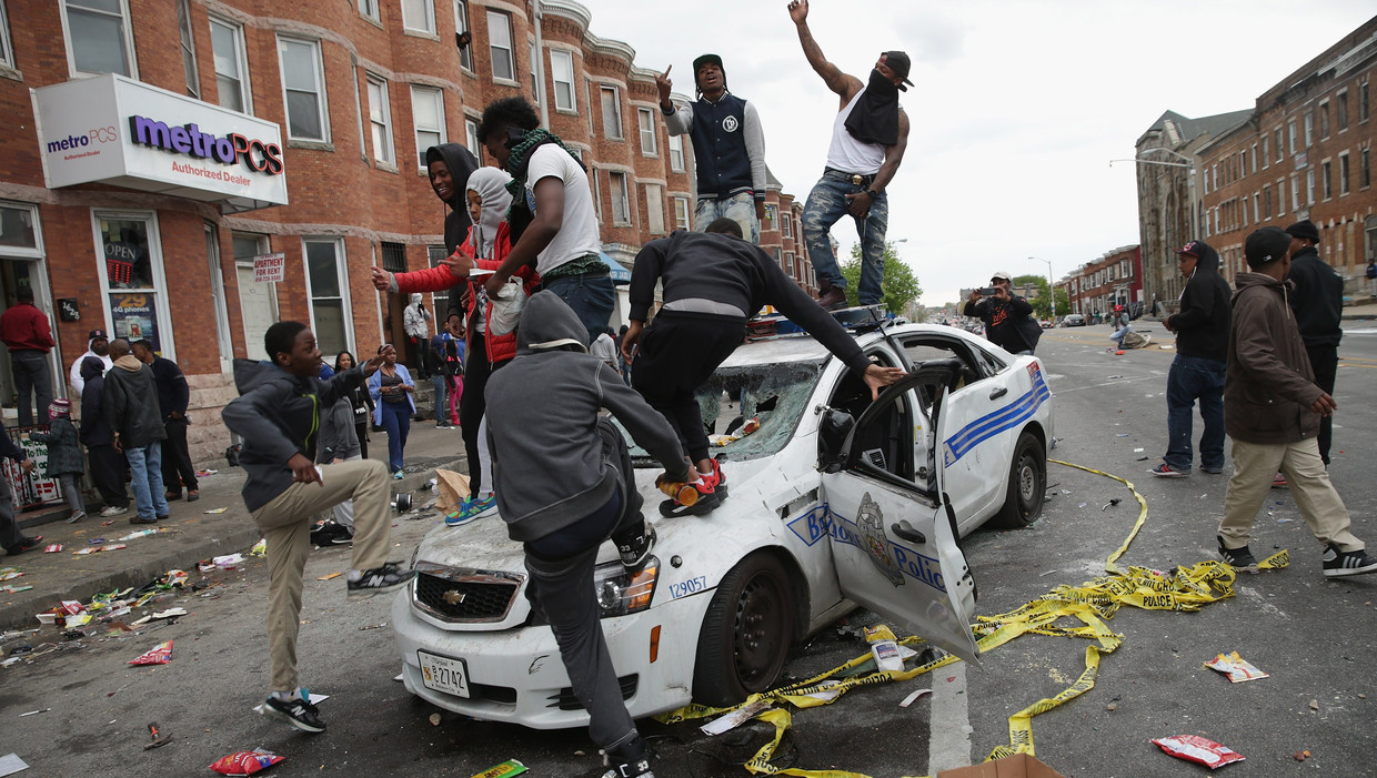 Mannen op een politiewagen in Baltimore. Het geweld keert zich voornamelijk tegen de politie. Beeld AFP