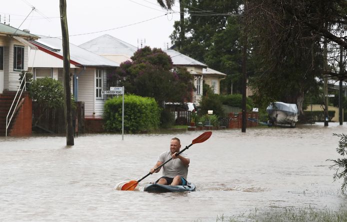 Een man kayakt door een overstroomde straat.