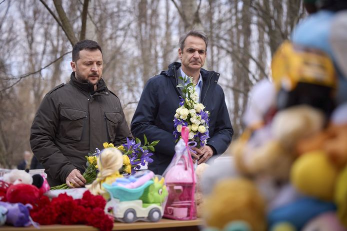 Zelensky en Mitsotakis bij een berg van beertjes en speelgoed vlakbij een flatgebouw in Odessa gisteren. Zaterdag kwamen twaalf mensen om na een Russische drone-aanval op het appartementsgebouw, onder wie vijf kinderen.