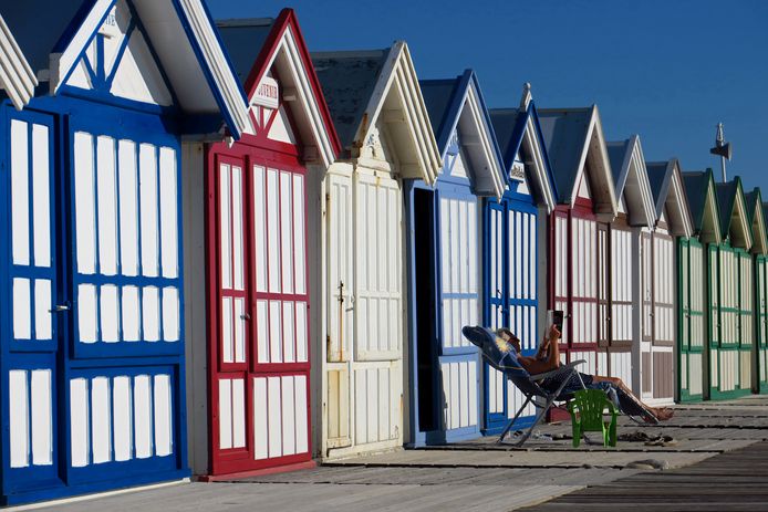 Een vrouw leest een boek voor een rij strandhuisjes in Cayeux-sur-mer in het noorden van Frankrijk.