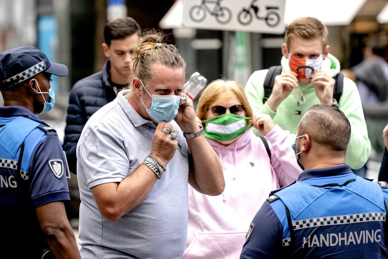 Een Nederlandse politieagent maant shoppers aan hun mondmasker te dragen. 