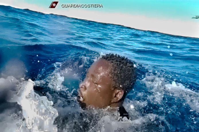 Een migrant wordt door de Italiaanse kustwacht uit het water gered.