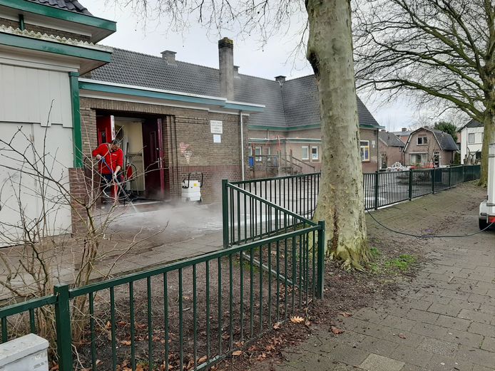 Een medewerker van Dolmans spuit de stoep voor de ingang van de Emmaschool schoon.