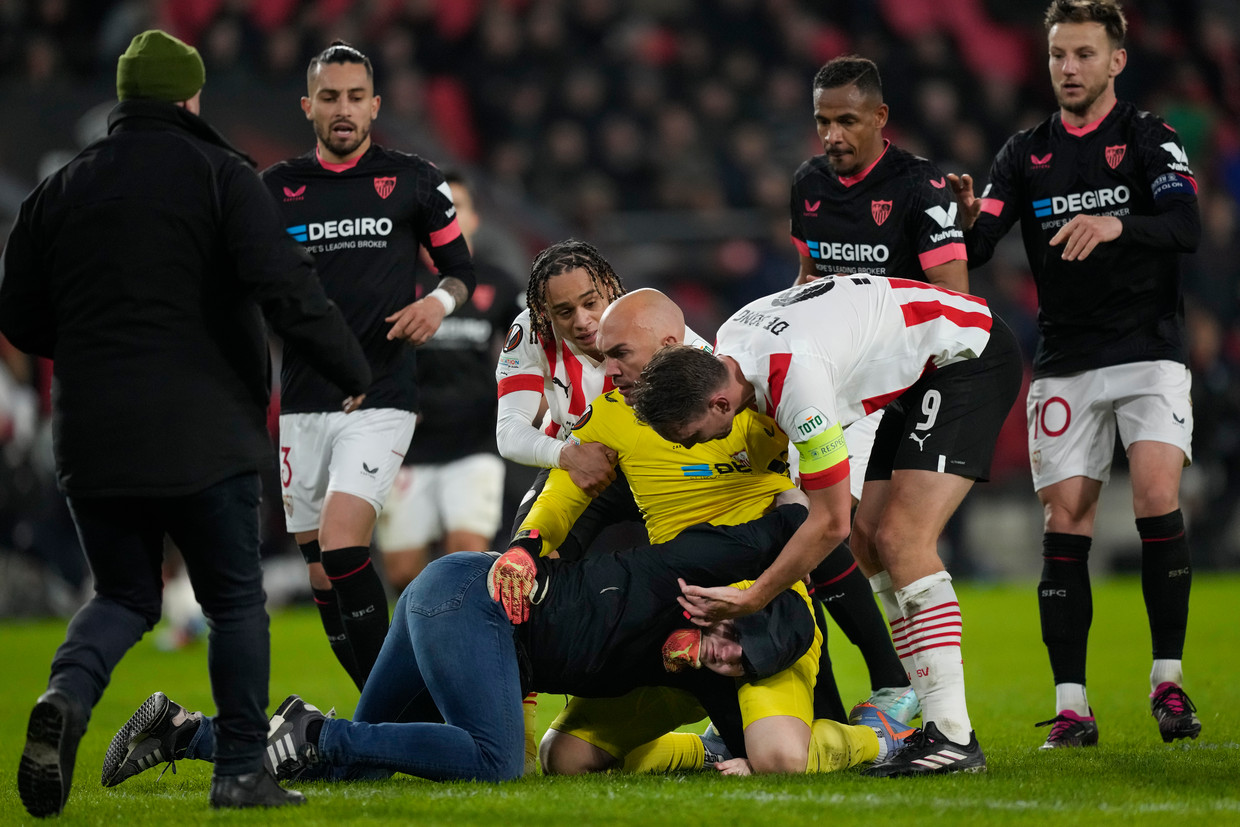 Sevilla-keeper Marko Dmitrovic houdt een PSV-supporter die hem belaagde in bedwang, daarbij geassisteerd door onder meer Xavi Simons en Luuk de Jong.  Beeld AP
