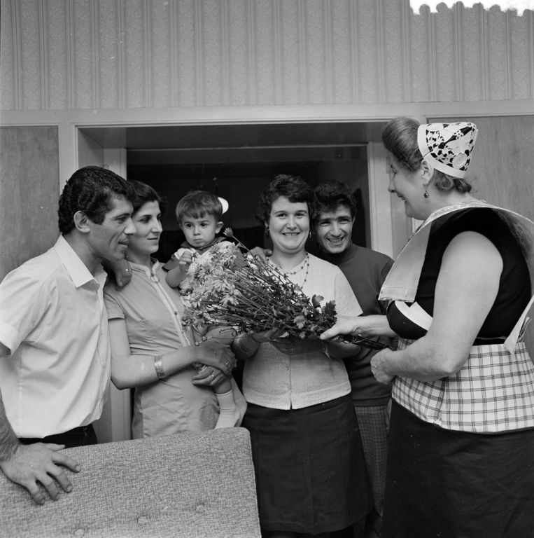 1968: Twee Turkse gastarbeiders in Spakenburg zijn herenigd met hun vrouwen. Een in klederdracht gestoken buurtgenote brengt een bos bloemen. Beeld anp