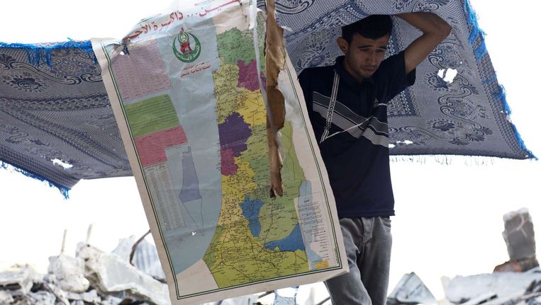 Een man tussen het puin in Gaza. Aan zijn kleed hangt een kaart van Israël en Palestina. Beeld ANP