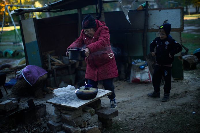 Vrouw haalt een pot eten van een geïmproviseerd fornuis naast haar kleinkind in Kivsharivka, Oekraïne.
