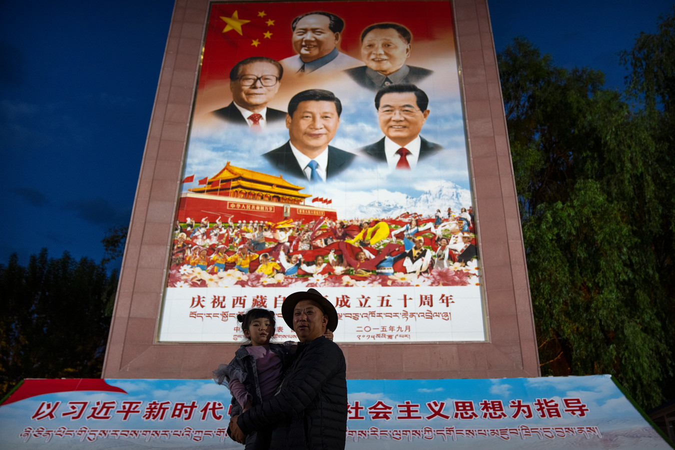 Un homme tient une fille dans ses bras alors qu'ils posent pour une photo devant une grande fresque représentant le président chinois Xi Jinping, en bas au centre, et d'autres dirigeants chinois sur une place publique au pied du palais du Potala à Lhassa, dans la région autonome du Tibet, dans l'ouest de la Chine. Le dirigeant chinois Xi Jinping a effectué une rare visite au Tibet alors que les autorités renforcent les contrôles sur la culture bouddhiste traditionnelle de la région himalayenne, accompagnés d'une accélération du développement économique et de la modernisation des infrastructures.