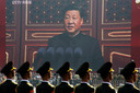 Chinese soldaten kijken tijdens een militaire parade naar een gigantisch scherm, terwijl Xi Jinping een toespraak houdt.