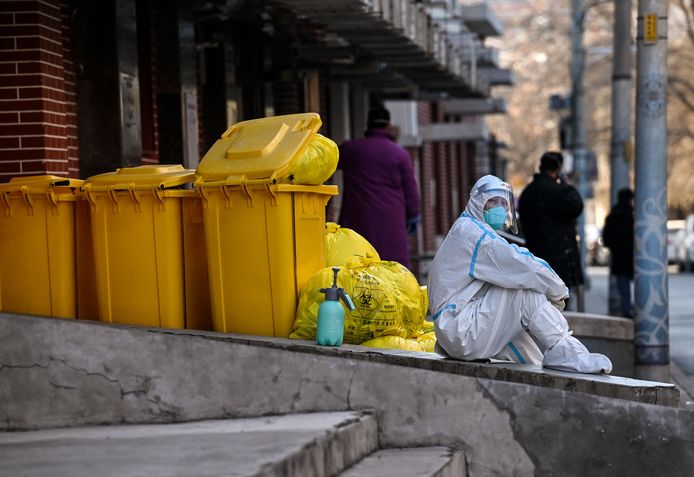 Een gezondheidswerker zit naast medisch afval buiten een koortskliniek in Peking.