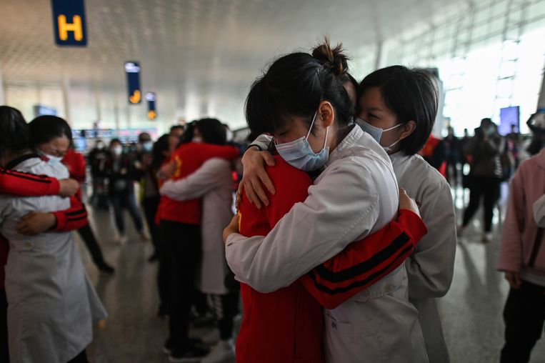 Medische professionals uit de provincie Jilin (in het rood) omhelzen hun collega’s uit Wuhan na samen te hebben gewerkt in de strijd tegen het coronavirus. Ze namen donderdag deel aan een korte ceremonie tijdens de heropening van het vliegveld in Wuhan. Beeld AFP